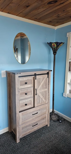 Un aparador de madera con cajones y un espejo, una lámpara de pie alta y una pared azul.