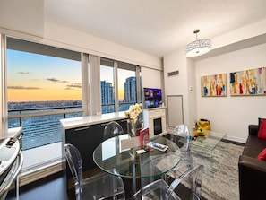 A modern living room with a glass dining table, clear chairs, a sofa, a TV, and artwork on the wall. - Commerce Suites and Stays (Vaughan)