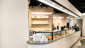 A modern cafe with a counter displaying pastries, a coffee machine, and a menu board. - Commerce Suites and Stays (Vaughan)