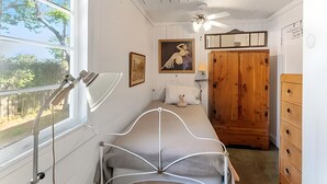 A bedroom with a bed, a ceiling fan, a window with a view, a wooden wardrobe, and a dresser. - The Flamingo Flat — Artsy Retreat 10 Min to Beach (Gulfport)