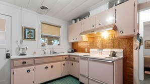 A kitchen with white cabinets, a window with blinds, a green mat, and a tiled backsplash. - The Flamingo Flat — Artsy Retreat 10 Min to Beach (Gulfport)