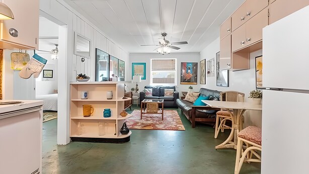 A modern living room with a sofa, coffee table, and a dining area with chairs. - The Flamingo Flat — Artsy Retreat 10 Min to Beach (Gulfport)