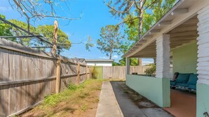A backyard with a wooden fence, a concrete pathway, and a covered patio area. - The Flamingo Flat — Artsy Retreat 10 Min to Beach (Gulfport)
