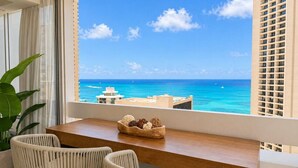 A balcony with a view of the ocean, a wooden table, two chairs, and a decorative bowl. - Waikiki Ocean Luxe Retreat | Panoramic Views (Honolulu)