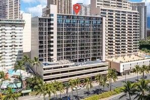 A multi-story hotel with a parking garage, palm trees, and a pool area. - Modern Waikiki Studio | Hilton Lagoon+Free Parking (Honolulu)