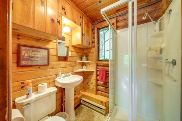 A wooden cabin bathroom with a toilet, sink, and shower.