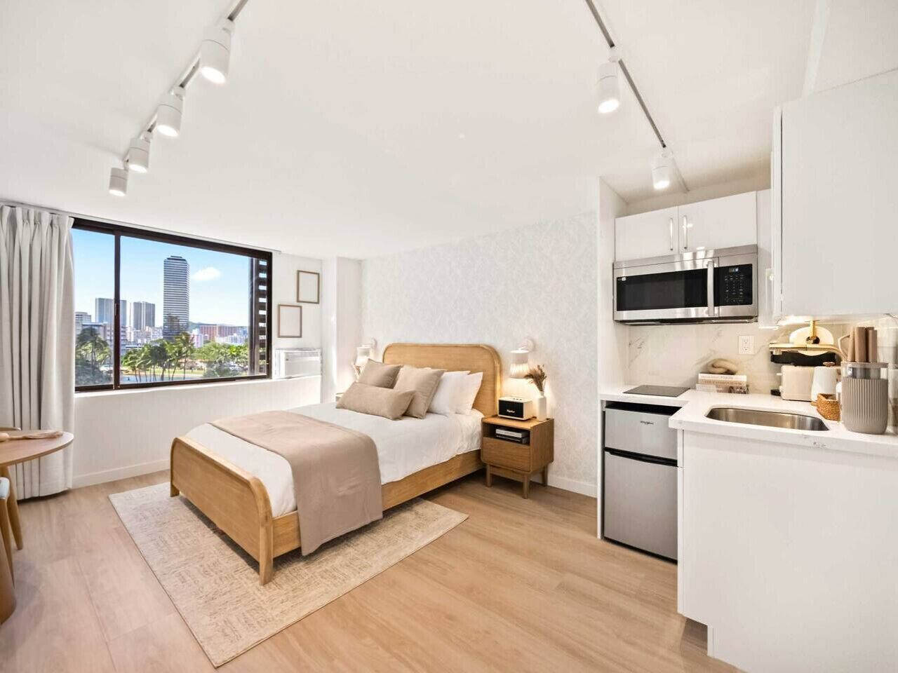 Een moderne hotelkamer met een bed, nachtkastje, lamp en uitzicht op een stadsbeeld.
