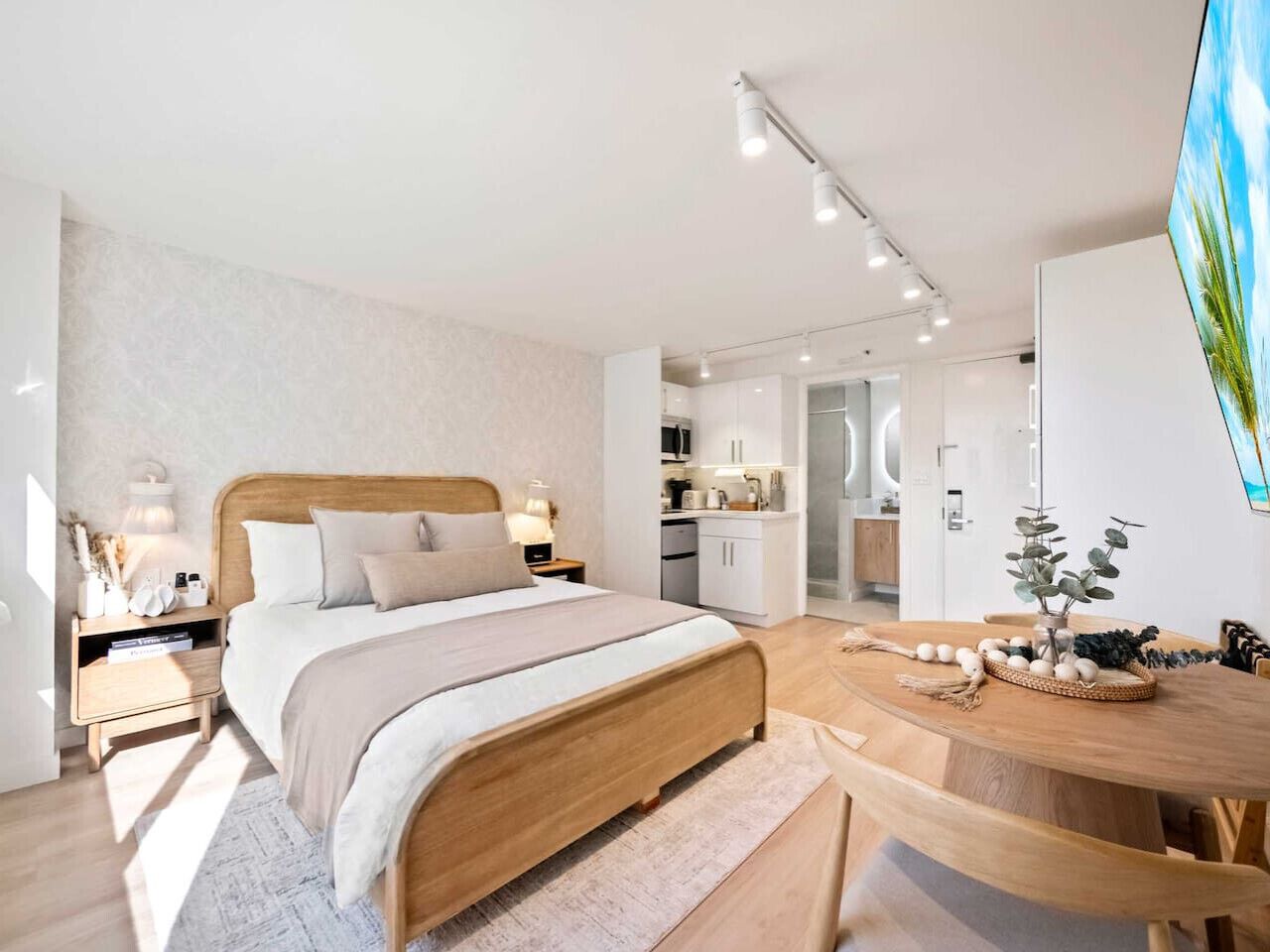 Ein modernes Schlafzimmer mit einem hölzernen Bett, Nachttischen, einem runden Esstisch und einer Küche im Hintergrund.