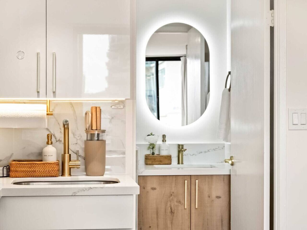 Een moderne badkamer met een marmeren wastafel, houten kastjes, een ronde spiegel en een handdoekrek.