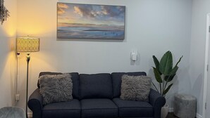 Un salon moderne avec un canapé foncé, un tableau, une lampe et une plante en pot.