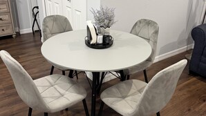 Une table de salle à manger ronde, accompagnée de quatre chaises, un vase avec des fleurs et un ensemble salière et poivrière.