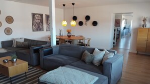 A modern living room with a sectional sofa, a dining area with a wooden table and chairs, and a kitchen in the background. - Holiday apartment by the coast on Ærø (Søby Ærø)