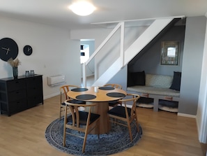A dining area with a round table, four chairs, a rug, a black dresser, and a staircase leading to a seating area.