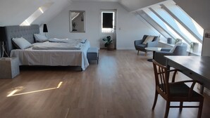A modern loft bedroom with a large bed, a desk, and a chair, featuring skylights and a view of the sky. - Holiday apartment by the coast on Ærø (Søby Ærø)