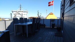 A deck with a table and chairs, a flag, and a building in the background. - Holiday apartment by the coast on Ærø (Søby Ærø)