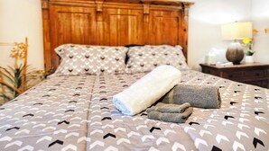 A bed with patterned bedding, a wooden headboard, and a bedside table with a lamp and a vase. - Spacious Desert Suite - Minutes to Phoenix Fun - Pet Friendly! (Avondale)