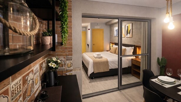 Una habitación de hotel moderna con una cama, un comedor y una zona de cocina con cafetera.