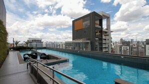 Un edificio moderno con piscina en la azotea, rodeado de un paisaje urbano.