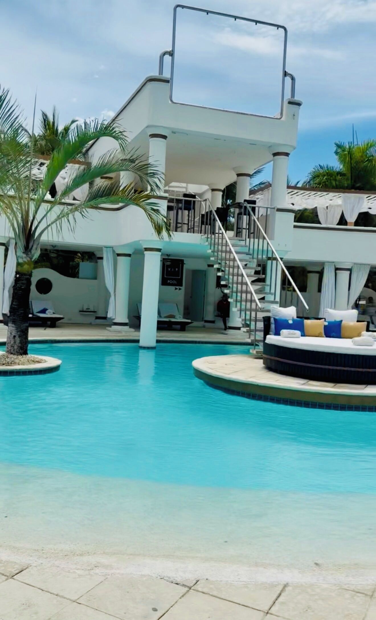 A pool area with a two-story building, a staircase, and lounge chairs.