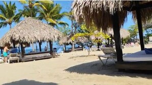 Een strand met rieten parasols, ligbedden en palmbomen.