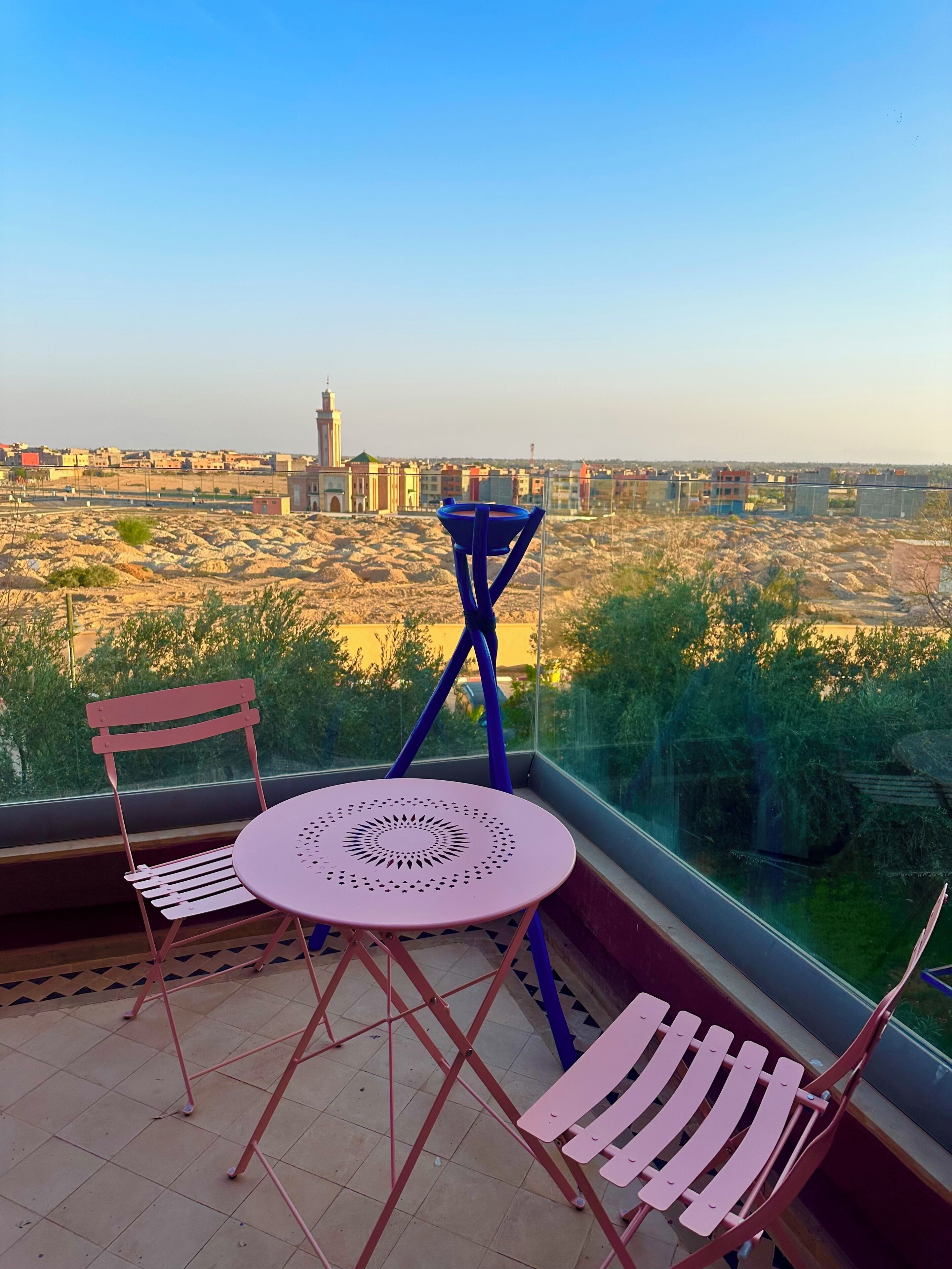 Ein Balkon mit Tisch und Stühlen, der einen Blick auf eine Stadt mit Gebäuden und einem entfernten Turm bietet.