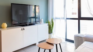 A modern living room with a flat-screen TV on a white cabinet, a small round table, a sofa, and a large window with curtains. - Studio 2 bedrooms for climbers in ALBARRACIN | FREE WIFI (AR)