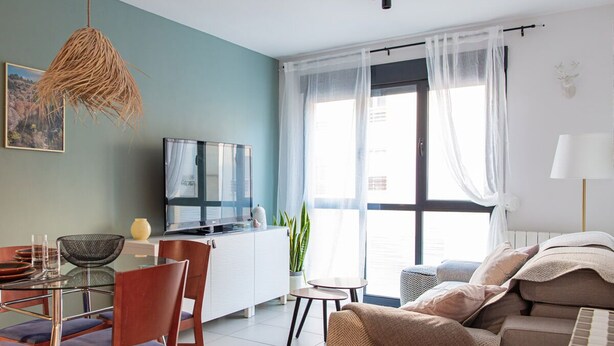 A modern living room with a sofa, TV, dining area, and a large window with sheer curtains. - Studio 2 bedrooms for climbers in ALBARRACIN | FREE WIFI (AR)