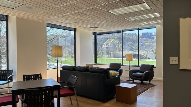 Ein modernes Wohnzimmer mit einer Couch, Sesseln, einem Esstisch und großen Fenstern mit Blick auf eine Brücke und einen Park.