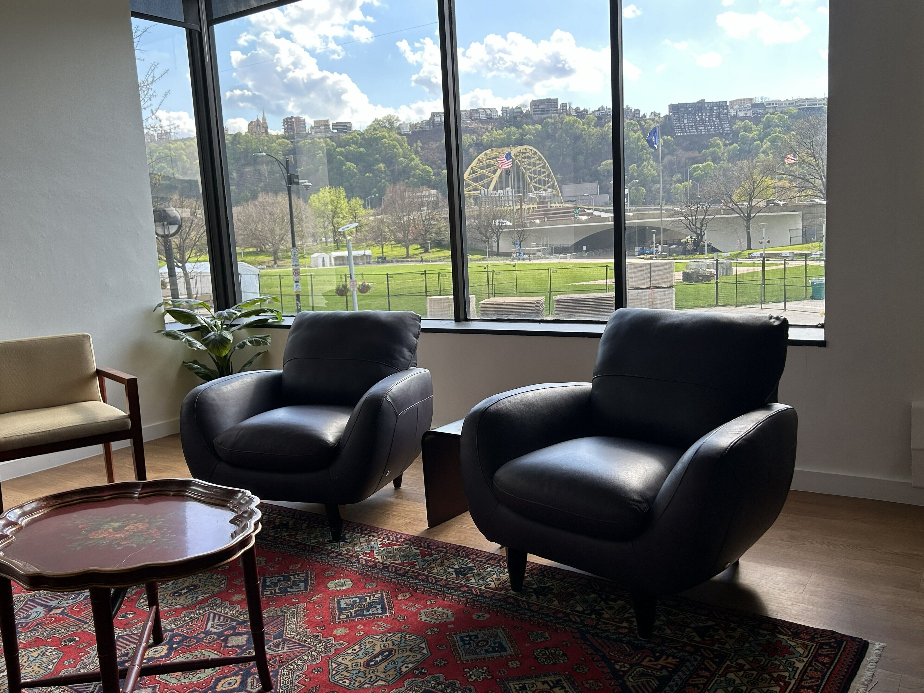 Quarto com duas poltronas de couro, uma mesa pequena e uma janela grande com vista para um parque e uma roda gigante.