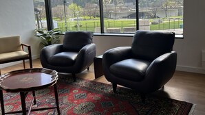Ein Zimmer mit zwei Ledersesseln, einem kleinen Tisch und einem großen Fenster mit Blick auf einen Park und ein Riesenrad.