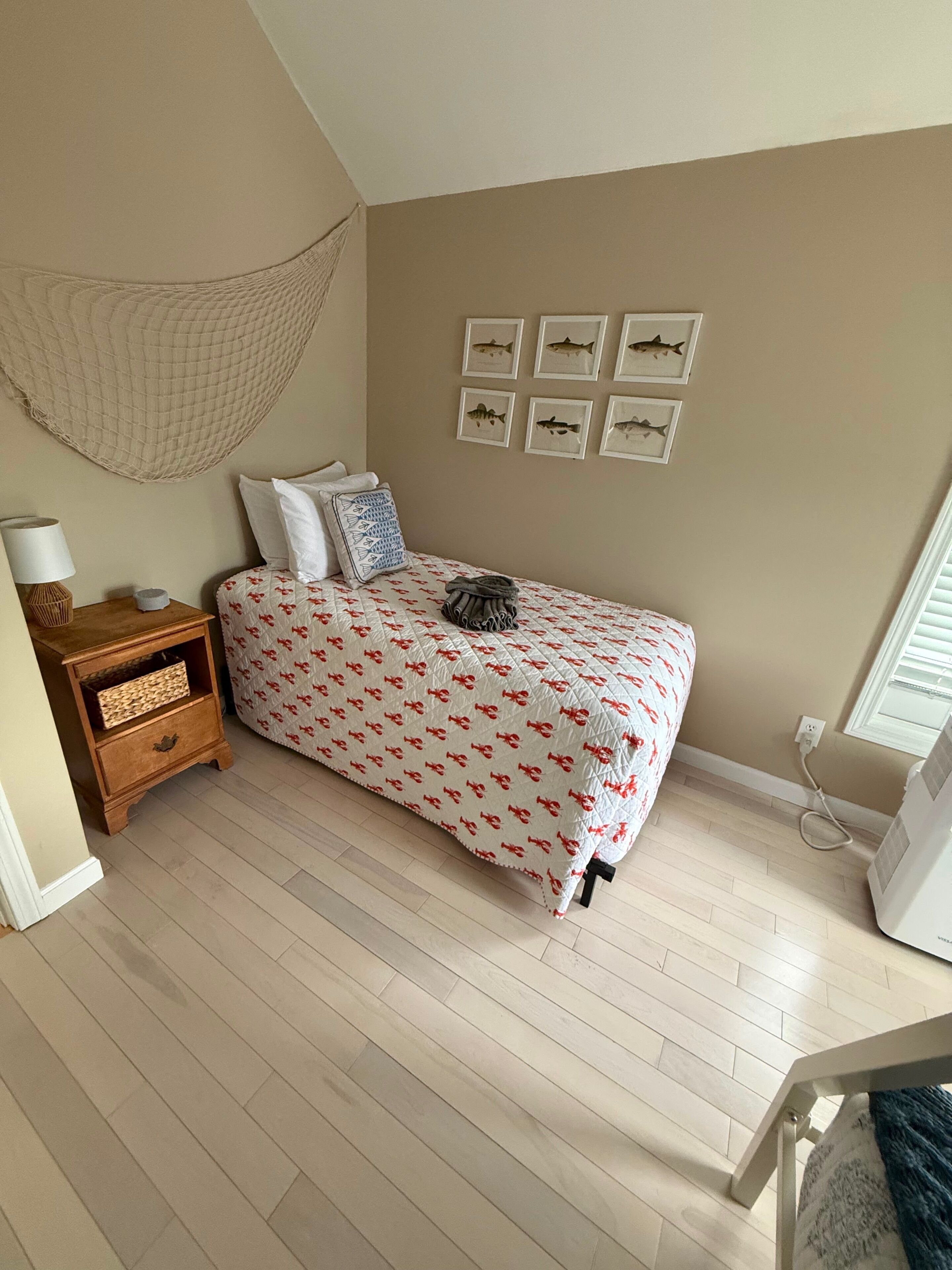 A bedroom with a bed, a nightstand, a wall-mounted hammock, and framed fish pictures.