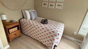 A bedroom with a bed, a nightstand, a wall-mounted hammock, and framed fish pictures.