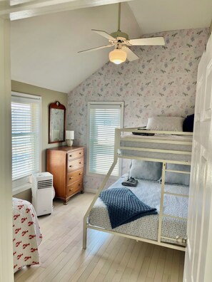 A bedroom with a bunk bed, a ceiling fan, a dresser, and a window with blinds.