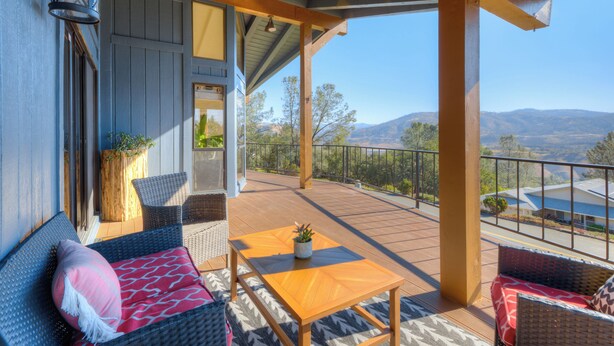 Une terrasse extérieure couverte, aménagée avec des meubles en osier, une table en bois et offrant une vue sur les montagnes.
