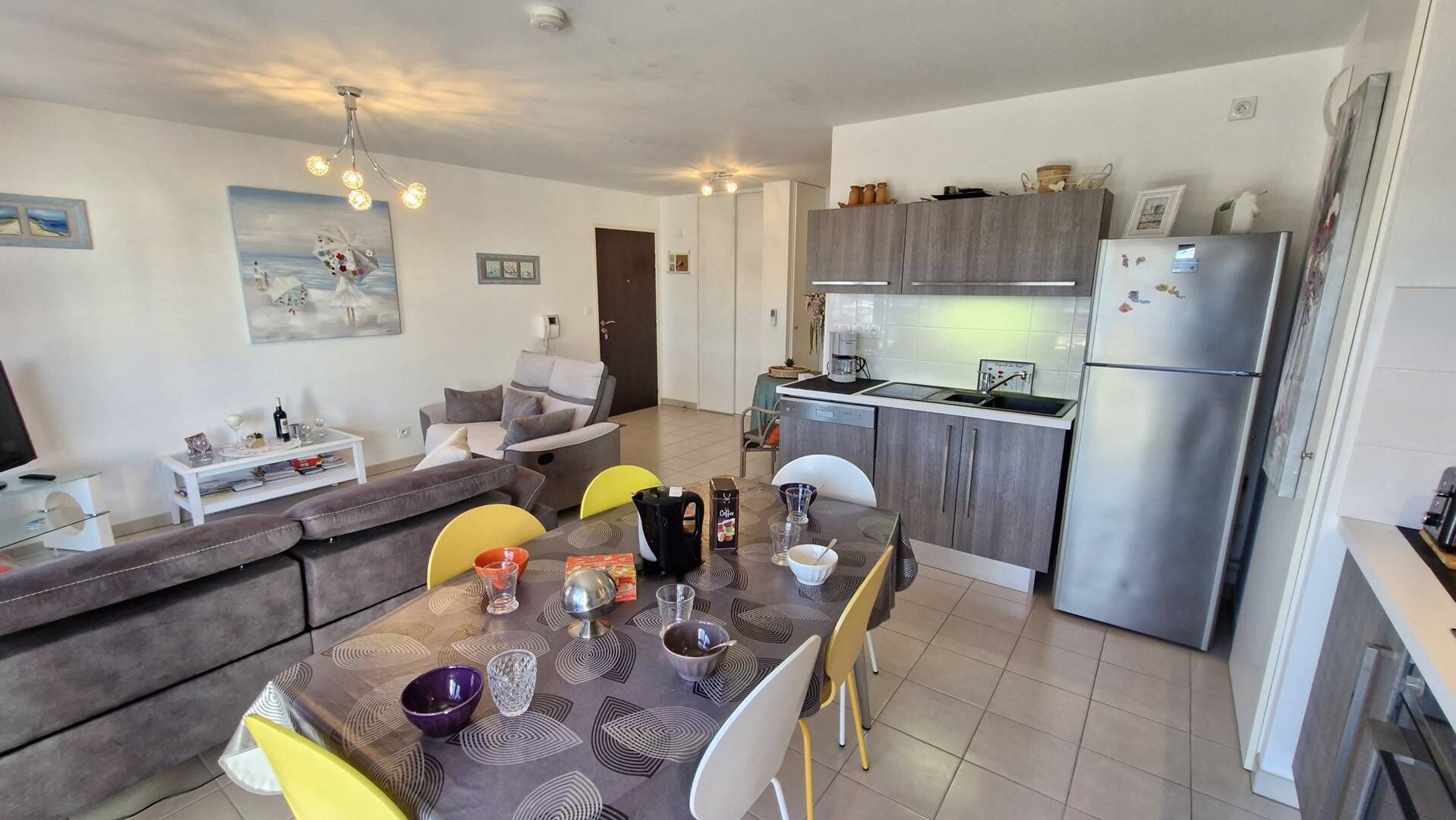 Une cuisine moderne équipée d’un four encastré, d’un réfrigérateur et d’un coin repas avec une table et des chaises.