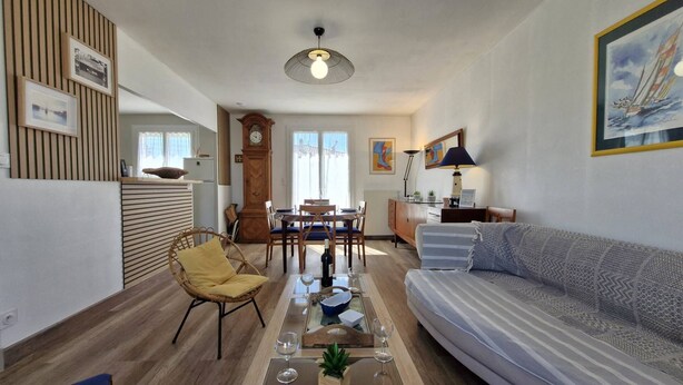 A living room with a sofa, a dining table, a chair, a clock, and a lamp. - Saint-Palais-sur-Mer – BRIGHT HOUSE – a relaxing escape between sea and nature (ST PALAIS SUR MER)