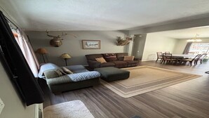 Ein Wohnzimmer mit Ecksofa, Hocker und einem Essbereich mit Tisch und Stühlen.