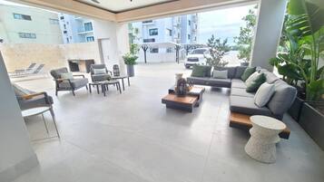A spacious living area with a sofa, coffee table, and chairs, large windows, and a view of buildings and a car.