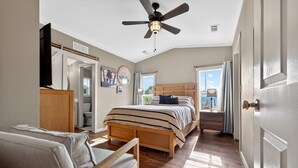Une chambre à coucher avec un lit, une chaise, un ventilateur de plafond, une commode et une porte.