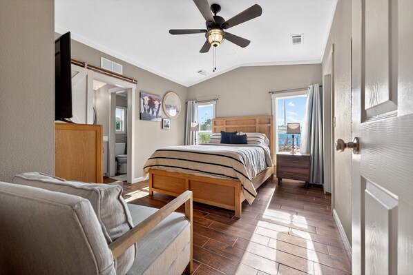 A bedroom with a bed, a chair, a ceiling fan, a dresser, and a door.
