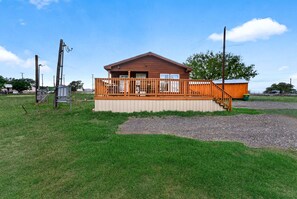 A wooden cabin with a balcony, a gravel area in front, and a clear sky.