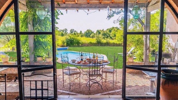 A patio with a table set for dining, overlooking a swimming pool and lush greenery. - Le Boucaou - SABONNERES (SABONNERES)