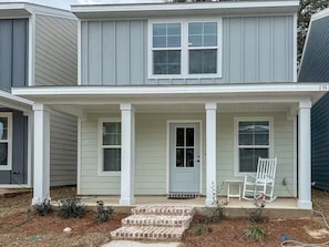 A two-story house with a front porch, a door, and a small garden area.