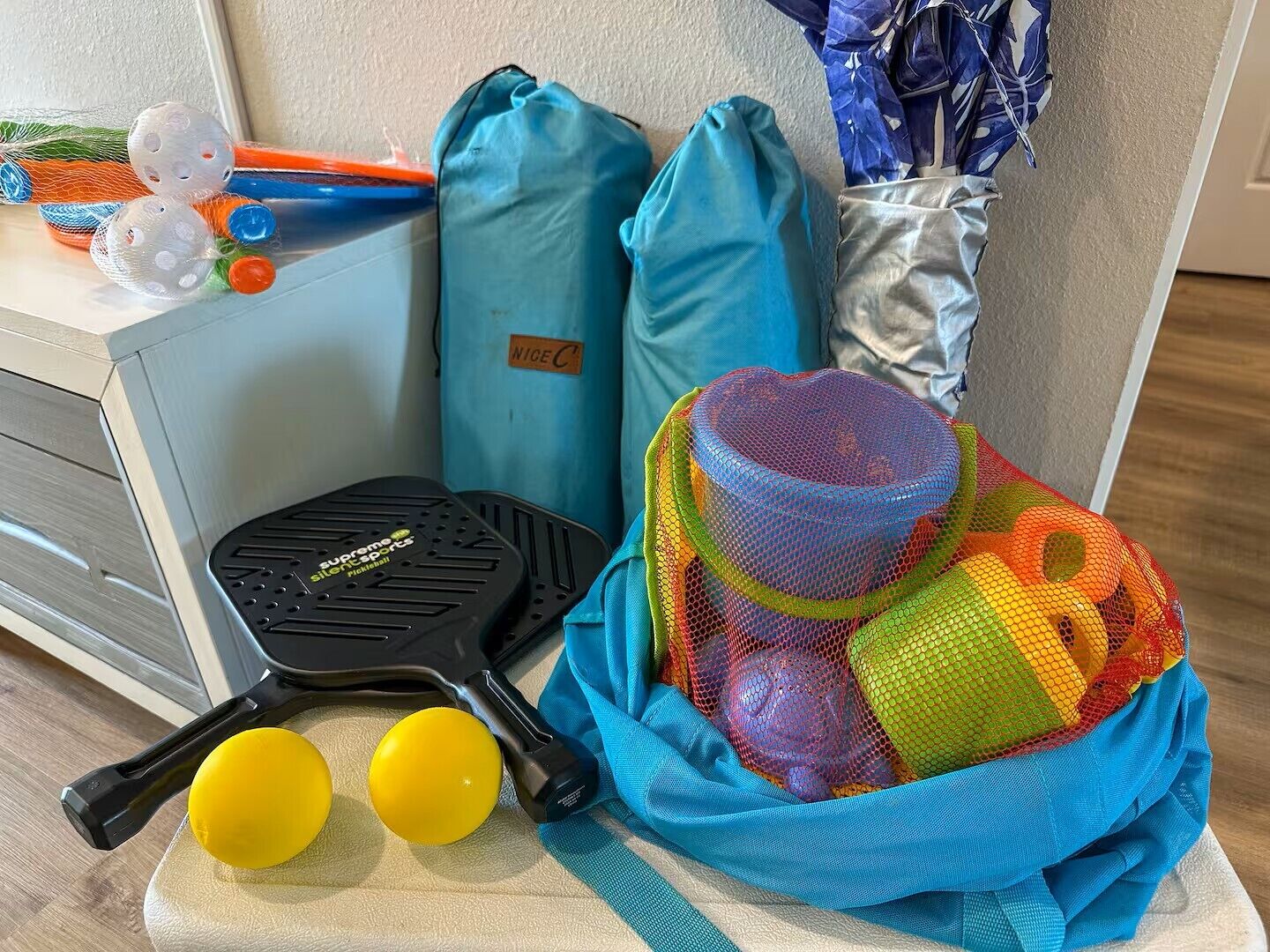 A sports equipment setup with a tennis racket, two yellow balls, and a bag of colorful sports balls.