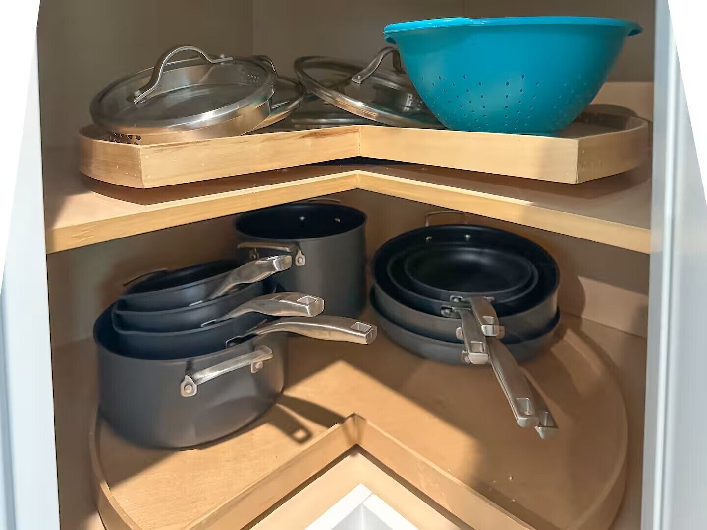 A kitchen with a wooden shelf holding pots, pans, and a blue colander.