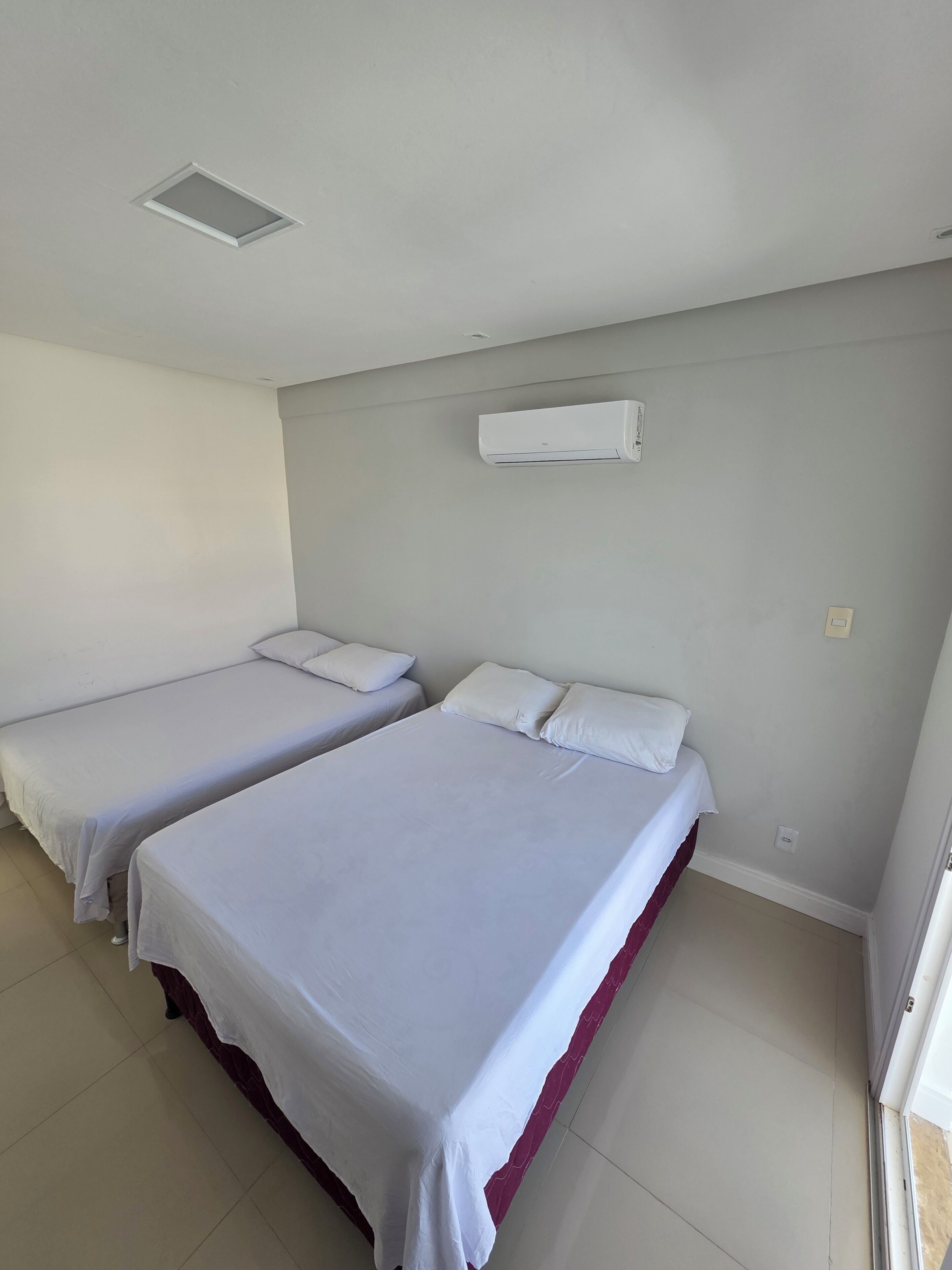 Habitación con dos camas individuales, aire acondicionado en la pared y una puerta que da a otra habitación.