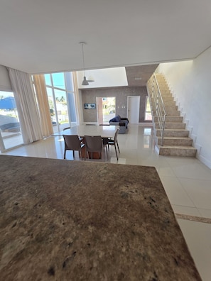 Un vaste espace de vie comprenant une table à manger, des chaises, un canapé, un escalier et de grandes fenêtres.