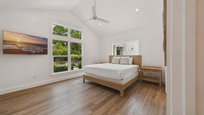 A bedroom with a bed, a nightstand, a ceiling fan, and a large window with a view of trees.