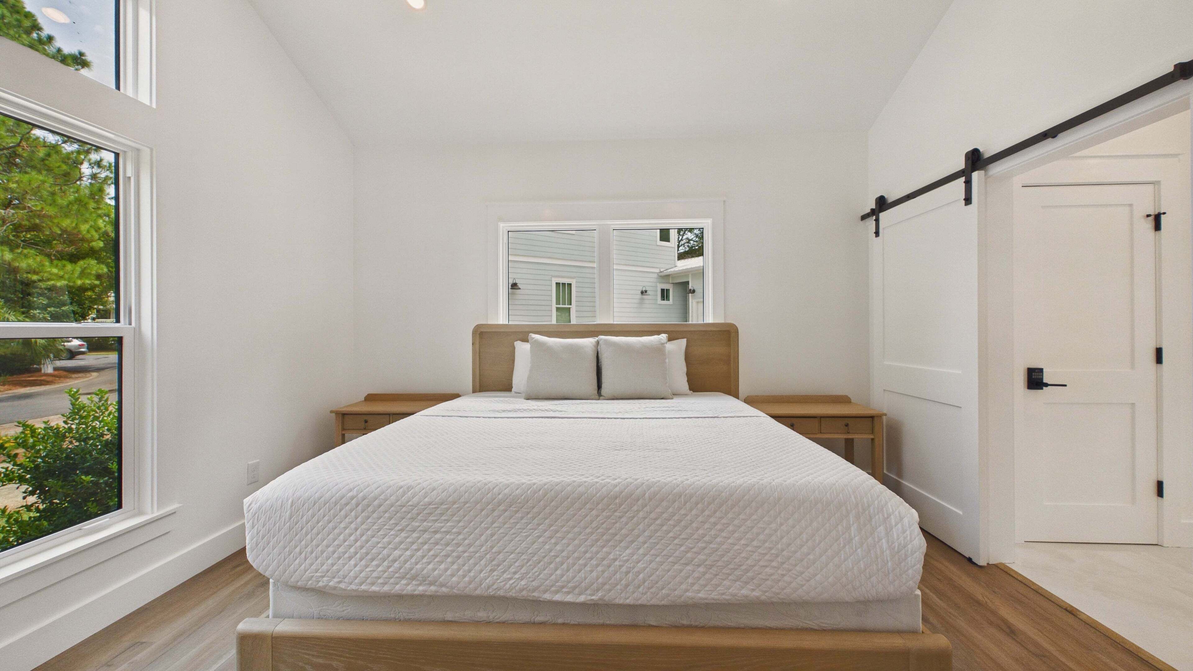 A bedroom with a large bed, a wooden nightstand, a window, and a door.