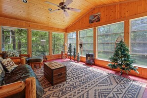 Interior acolhedor de uma cabana com janelas amplas, lareira e árvore de Natal.
